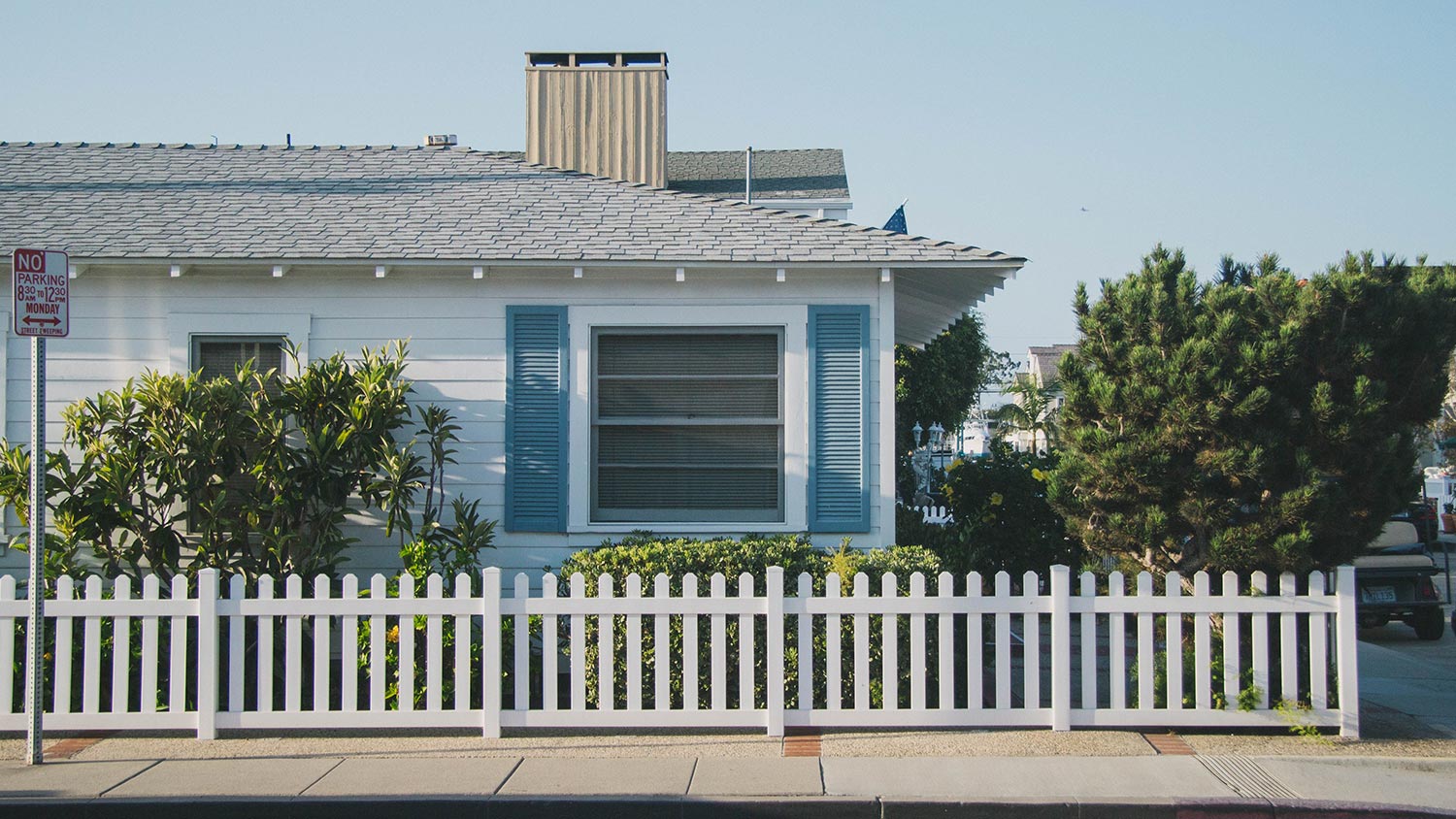 Outside view of a blue house with a white picket fence and leafy front garden.
